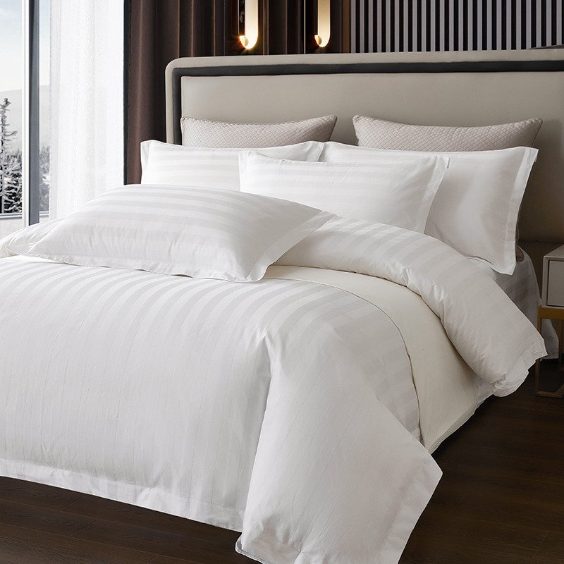 White pillows and striped white bedding arranged on a bed.